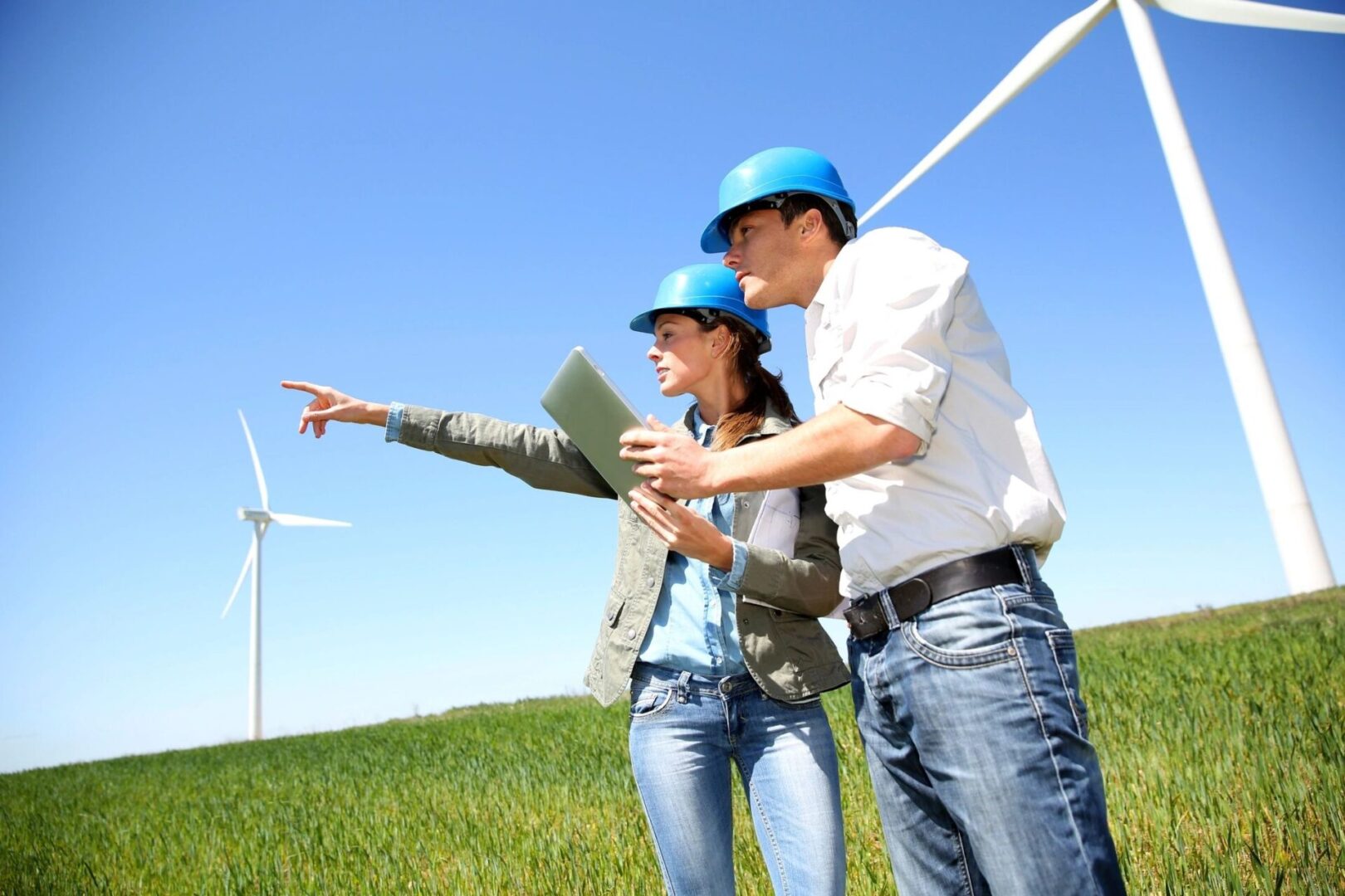 Two people standing in a field with wind turbines behind them.