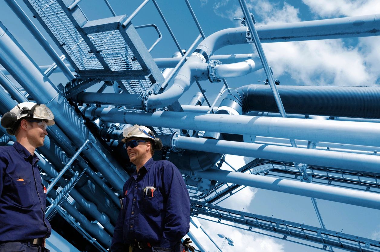 A man in blue shirt and white hat near pipes.